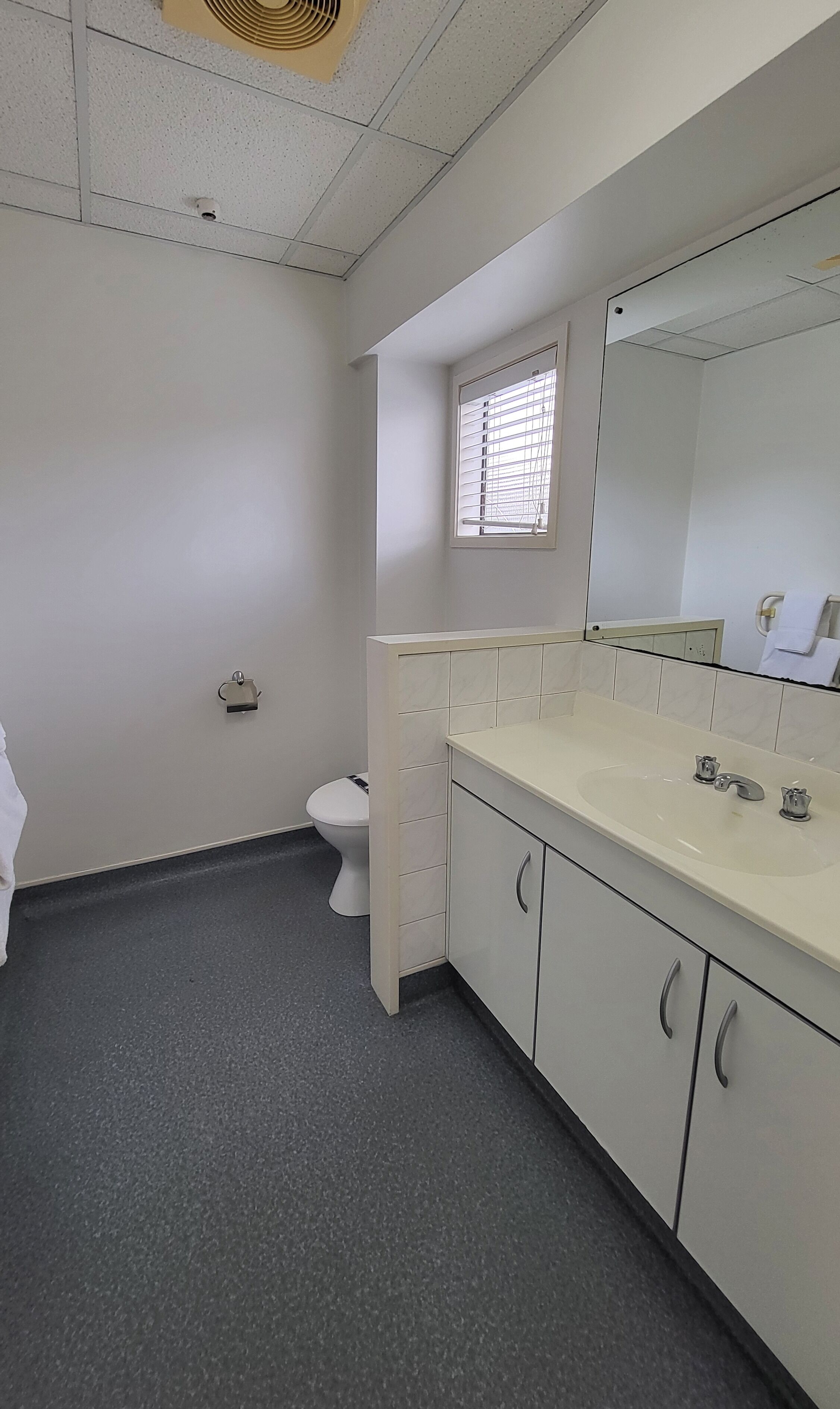 A bathroom with a toilet, a sink with a mirror, and a window with blinds.