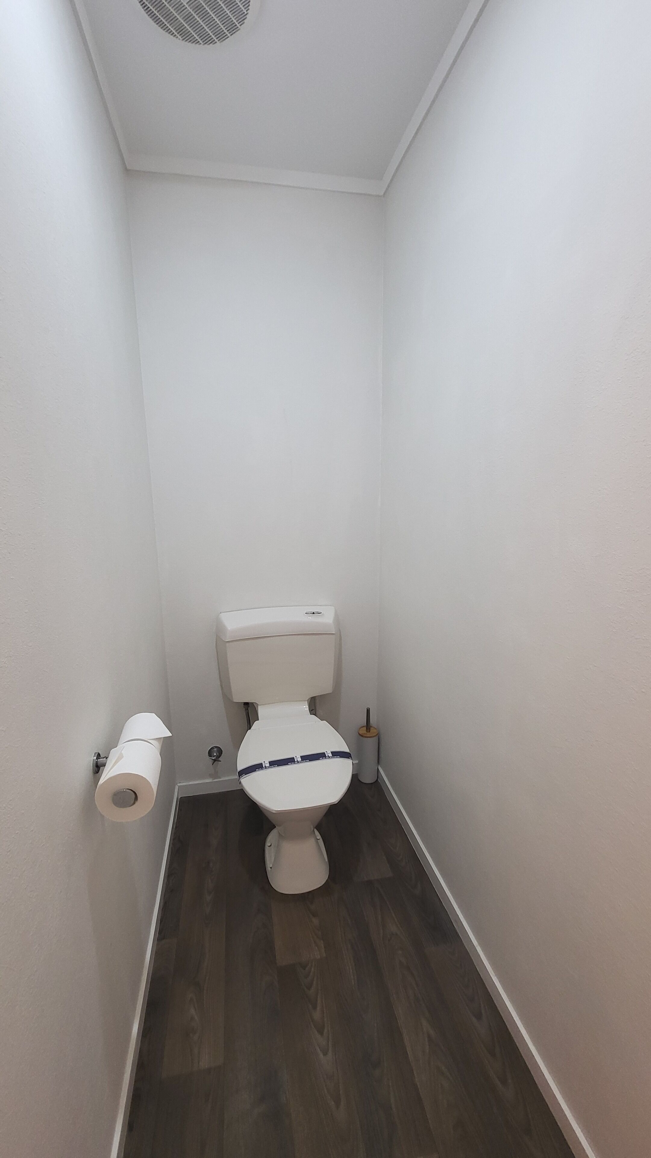 A small, narrow bathroom with a toilet, a toilet paper holder, and a toilet brush.