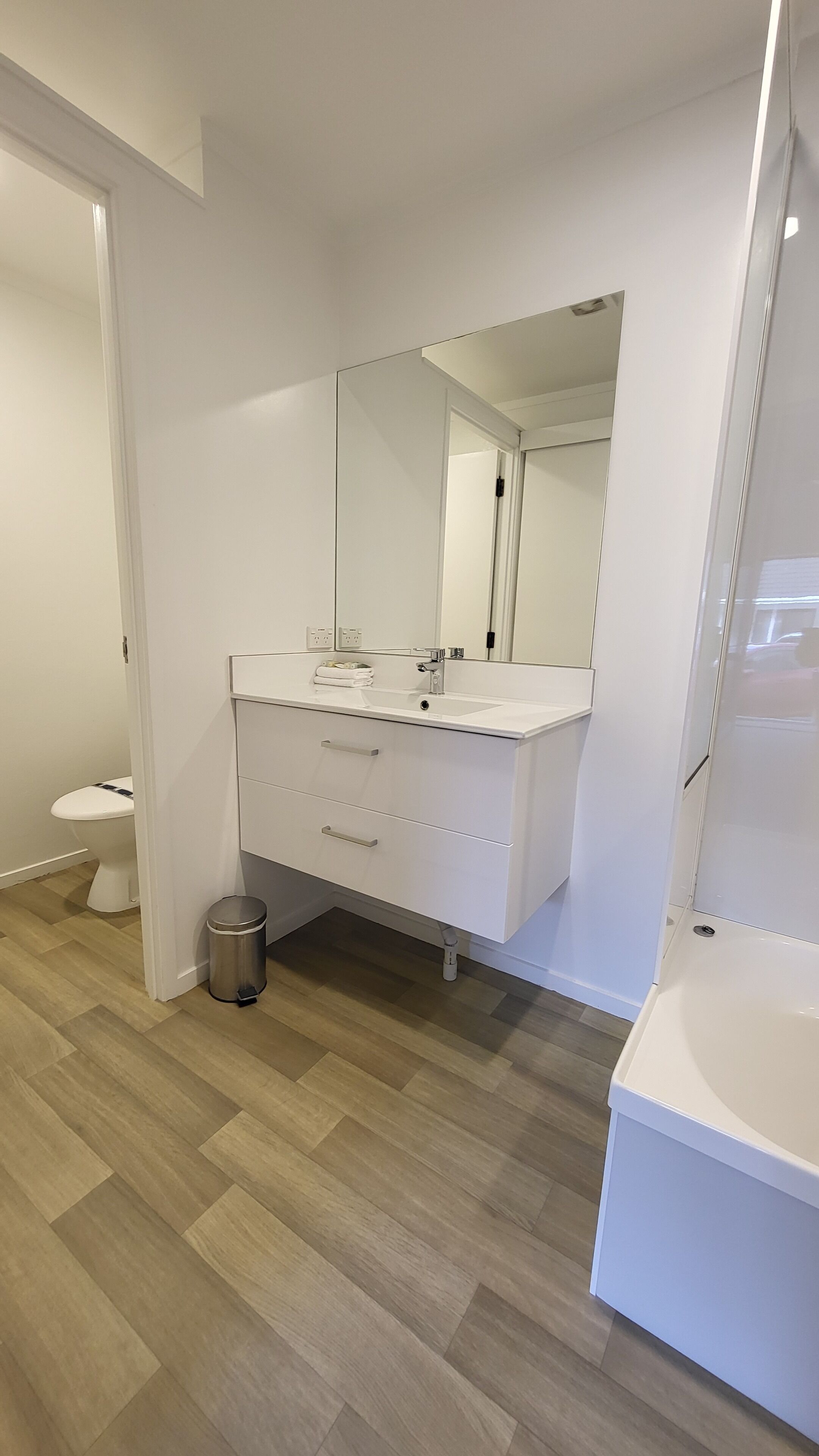Un baño moderno con tocador blanco, un espejo grande y un inodoro.