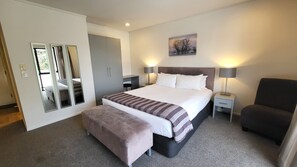 Ein ordentlich eingerichtetes Schlafzimmer mit einem großen Bett, Nachttischlampen, einem Sessel und einem Spiegel.