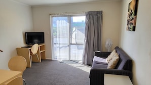 A modern living room with a flat-screen TV, a sofa, a dining table, and a large window with curtains. - Manukau Motor Lodge (Auckland)