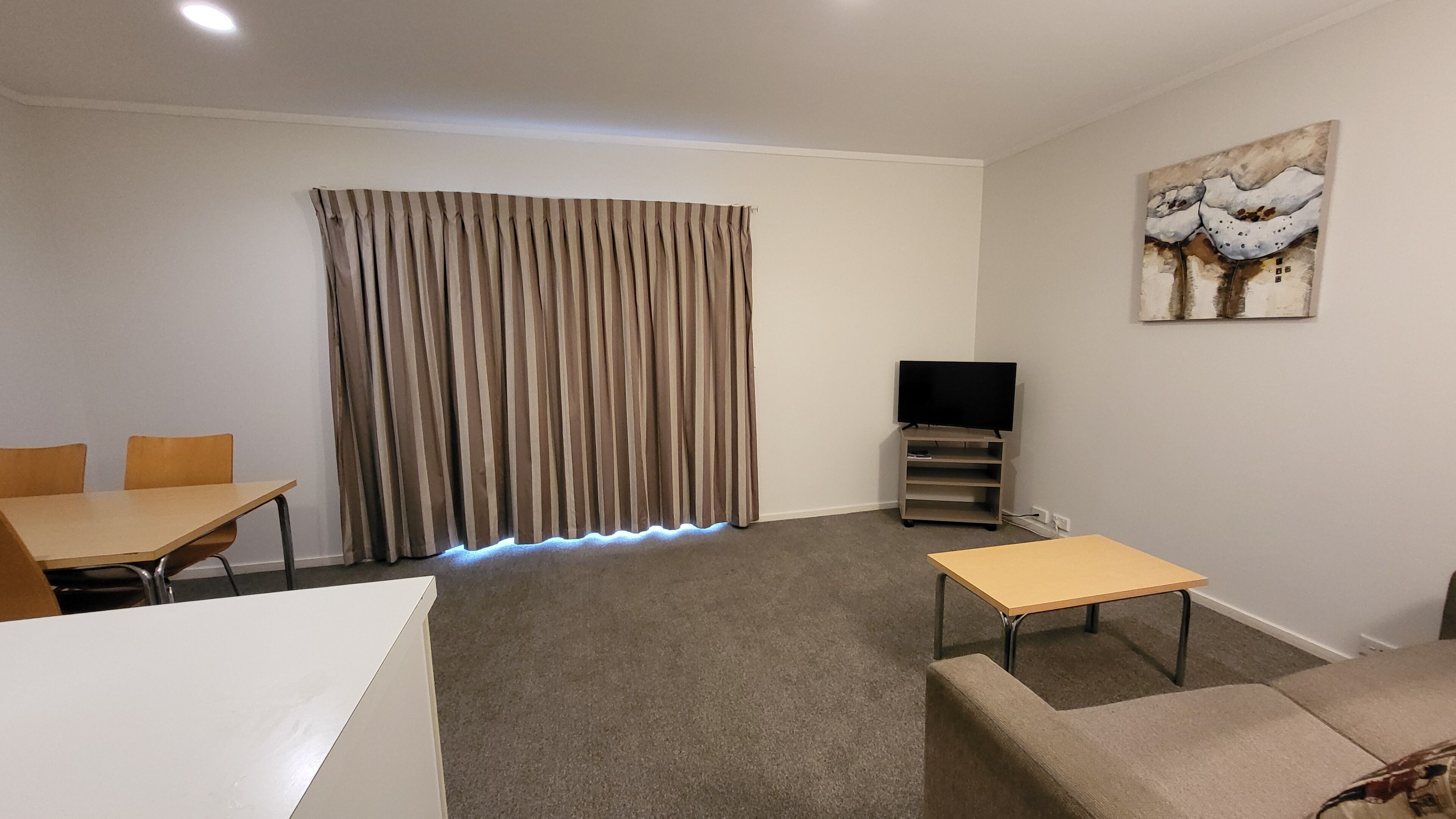 A living room with a flat-screen TV, a painting, a dining table with chairs, and a sofa.