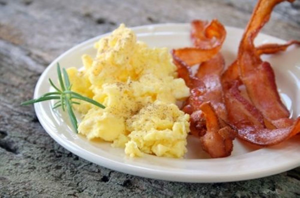 Un plato de huevos revueltos con tocino y una ramita de romero.