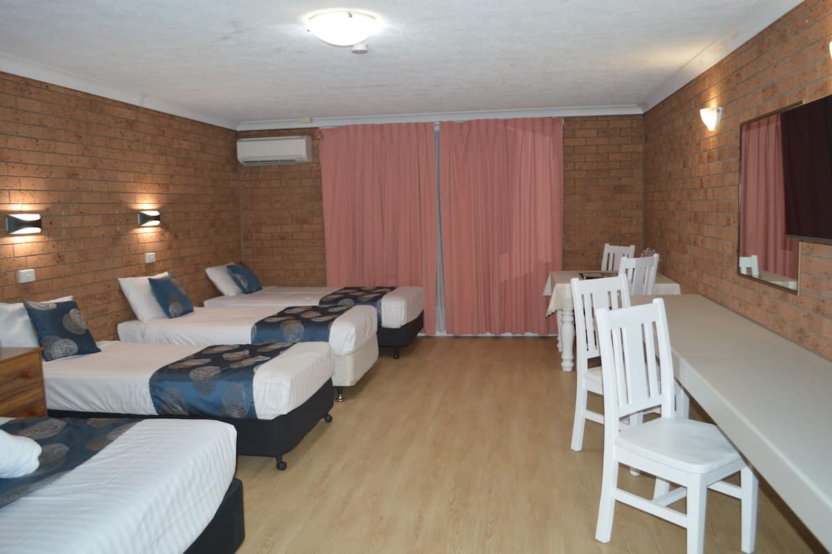 A hotel room with four single beds, a dining table with chairs, and a brick wall.