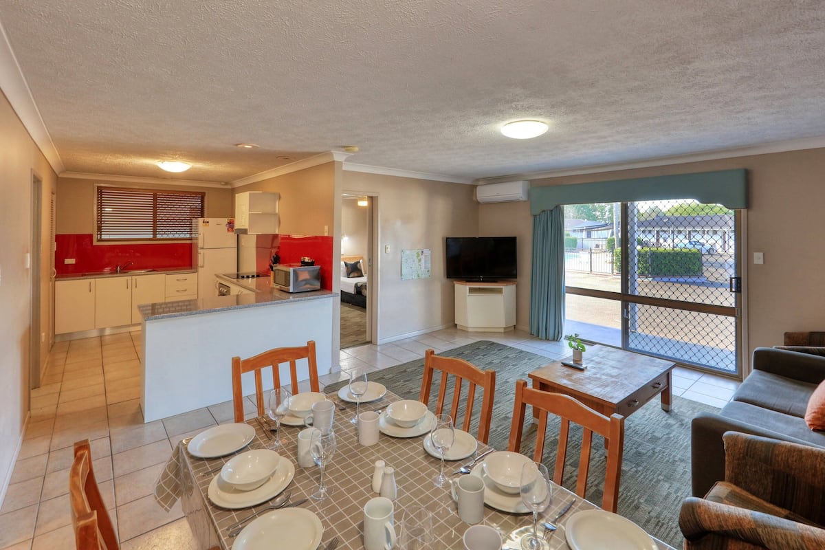 A compact apartment with a dining area, kitchenette, living room, and a large sliding glass door to the outside.