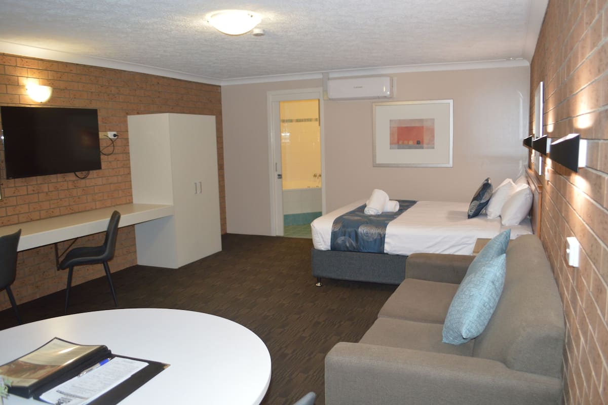 A hotel room with a bed, a desk, a chair, a couch, and a TV.