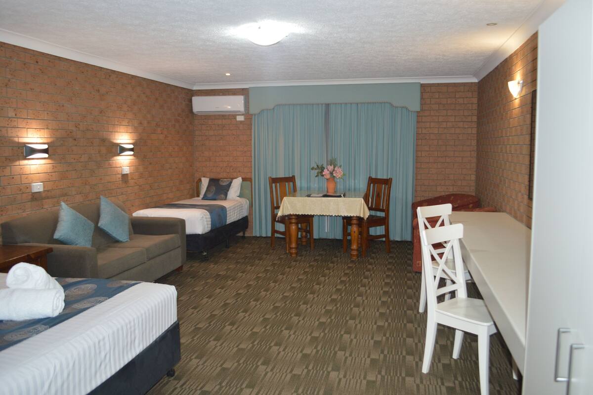A hotel room with a bed, a sofa, a dining table with chairs, and a brick wall.