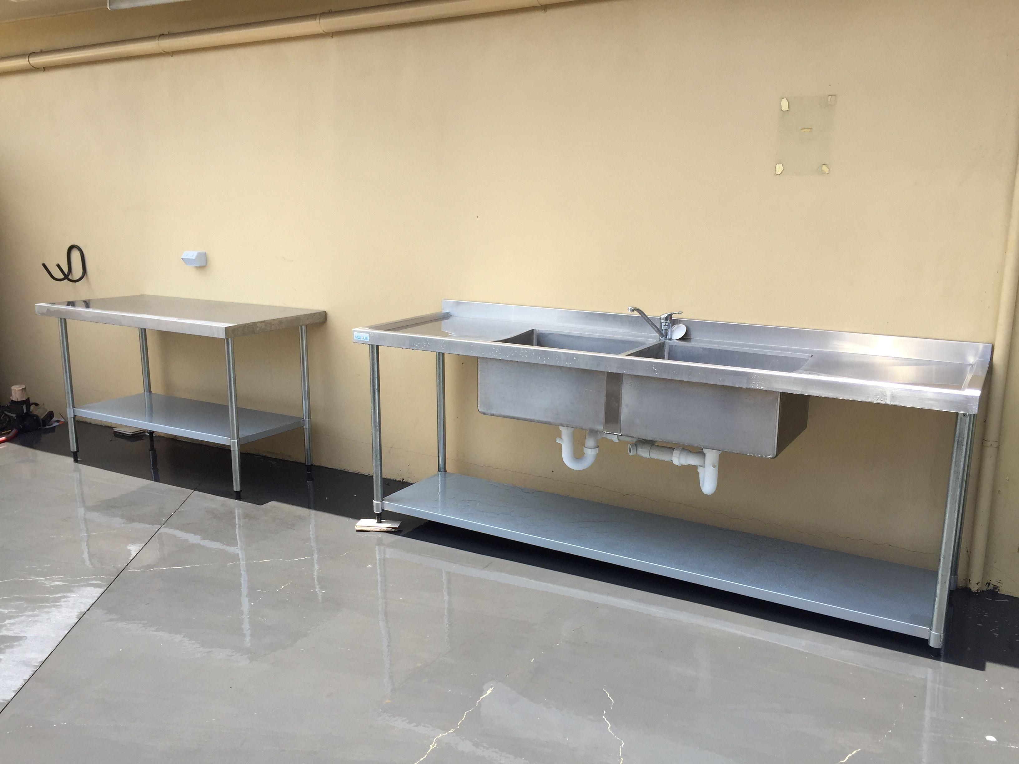 A clean, stainless steel kitchenette with a sink and a small table, likely in a hotel or similar accommodation.
