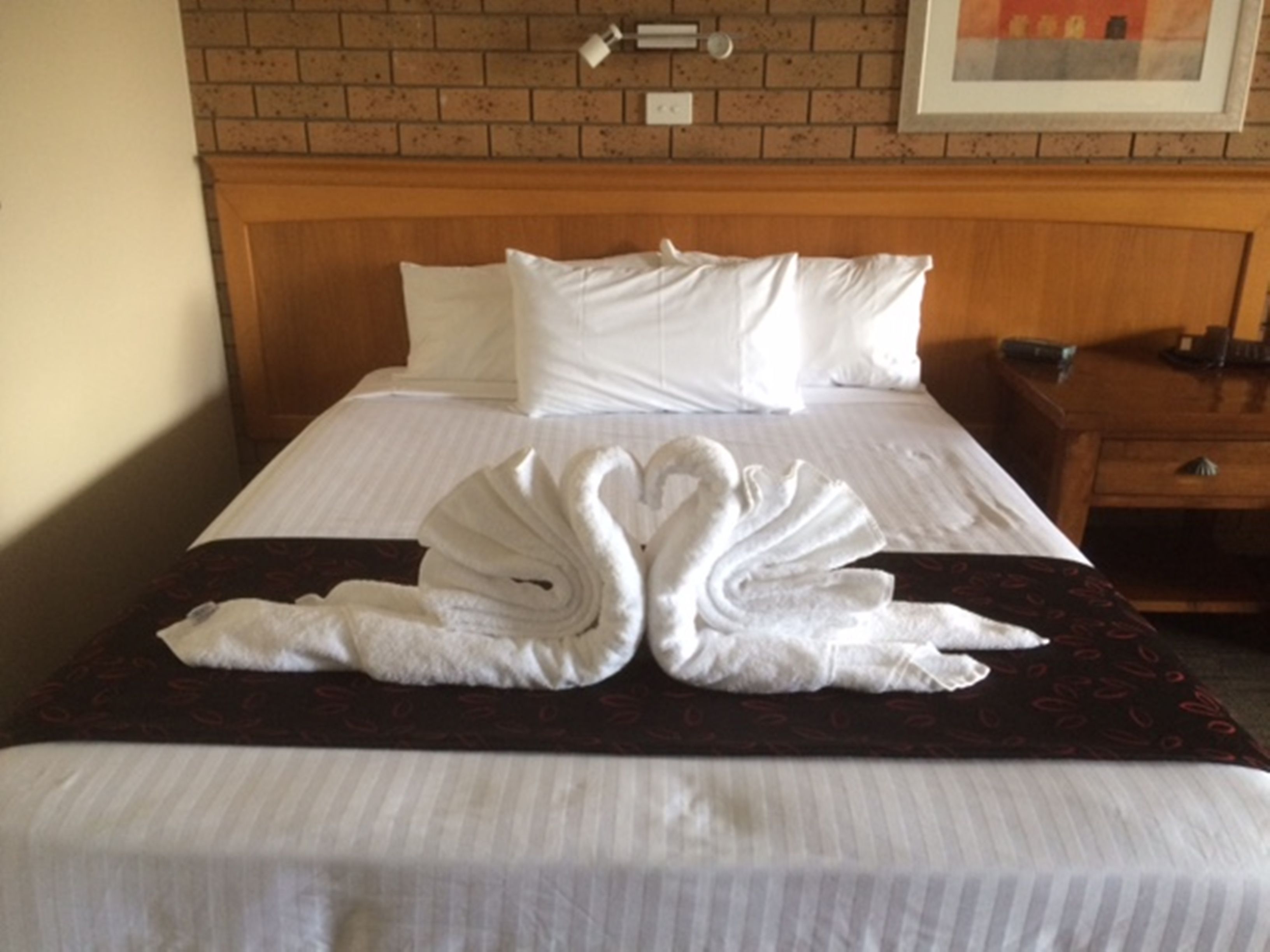 A neatly made bed with white linens, a wooden headboard, and a decorative towel arrangement on the bedspread.