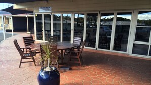 An outdoor patio with a round table and chairs, a large blue vase with a plant, and a sign for James Street Motor Inn. - James Street Motor Inn (South Toowoomba)