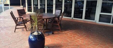 An outdoor patio with a round table and chairs, a large blue vase with a plant, and a sign for James Street Motor Inn.
