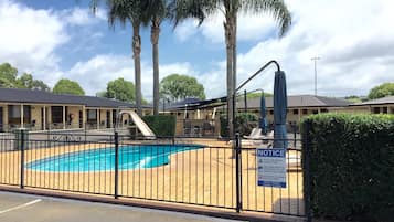 Zona de piscina con valla, cartel informativo y palmeras al fondo.