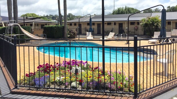 A swimming pool surrounded by a metal fence, with lounge chairs and a slide in the background. - James Street Motor Inn (South Toowoomba)
