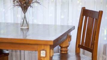 Una mesa de comedor de madera con un jarrón de flores secas, ubicada frente a una ventana con cortinas translúcidas.