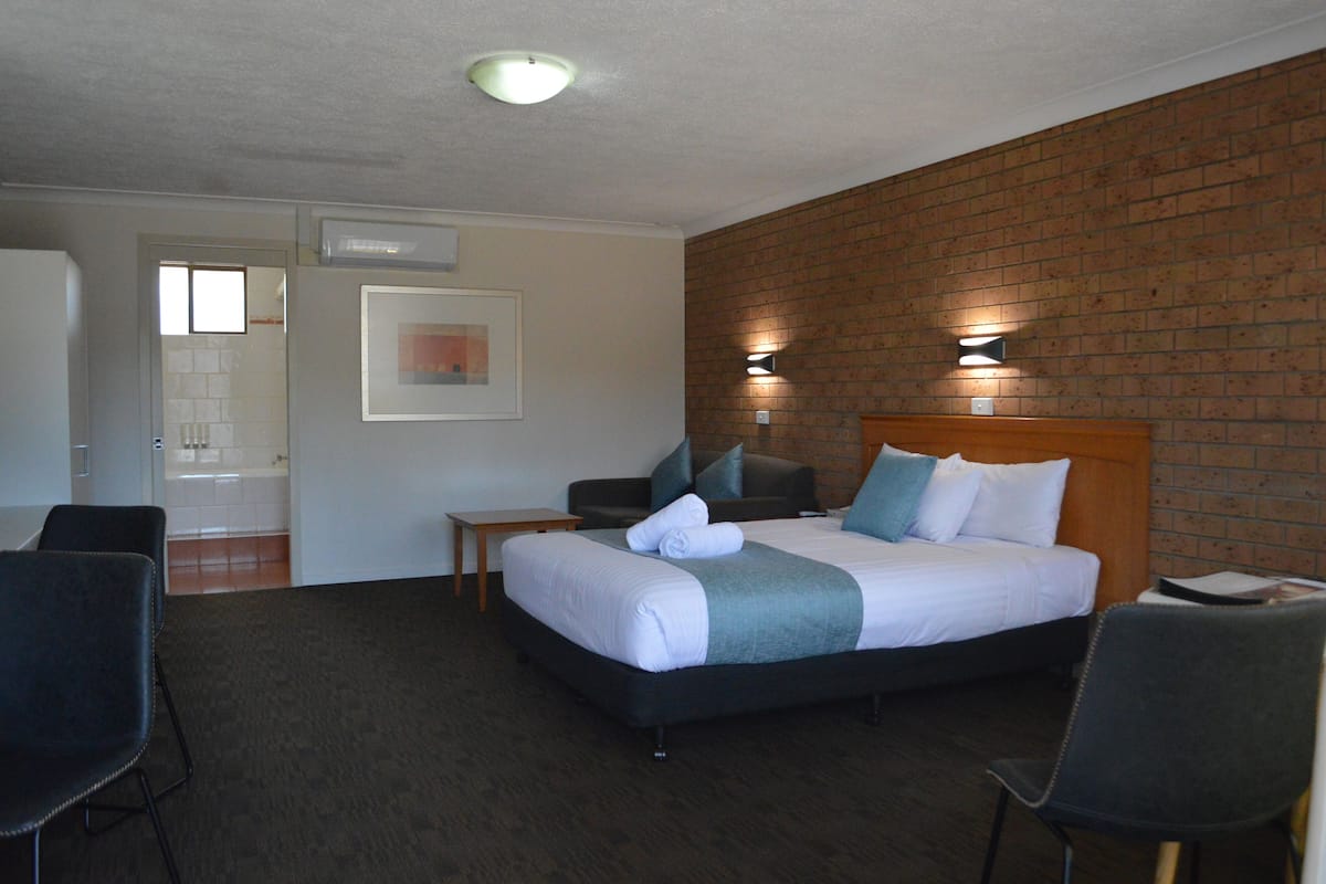 A hotel room with a bed, two chairs, a small table, and a brick wall.