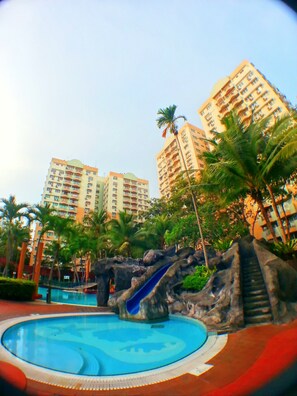 A swimming pool with a slide, surrounded by palm trees and a rocky area. - Malacca Hotel Apartment (Malacca City)