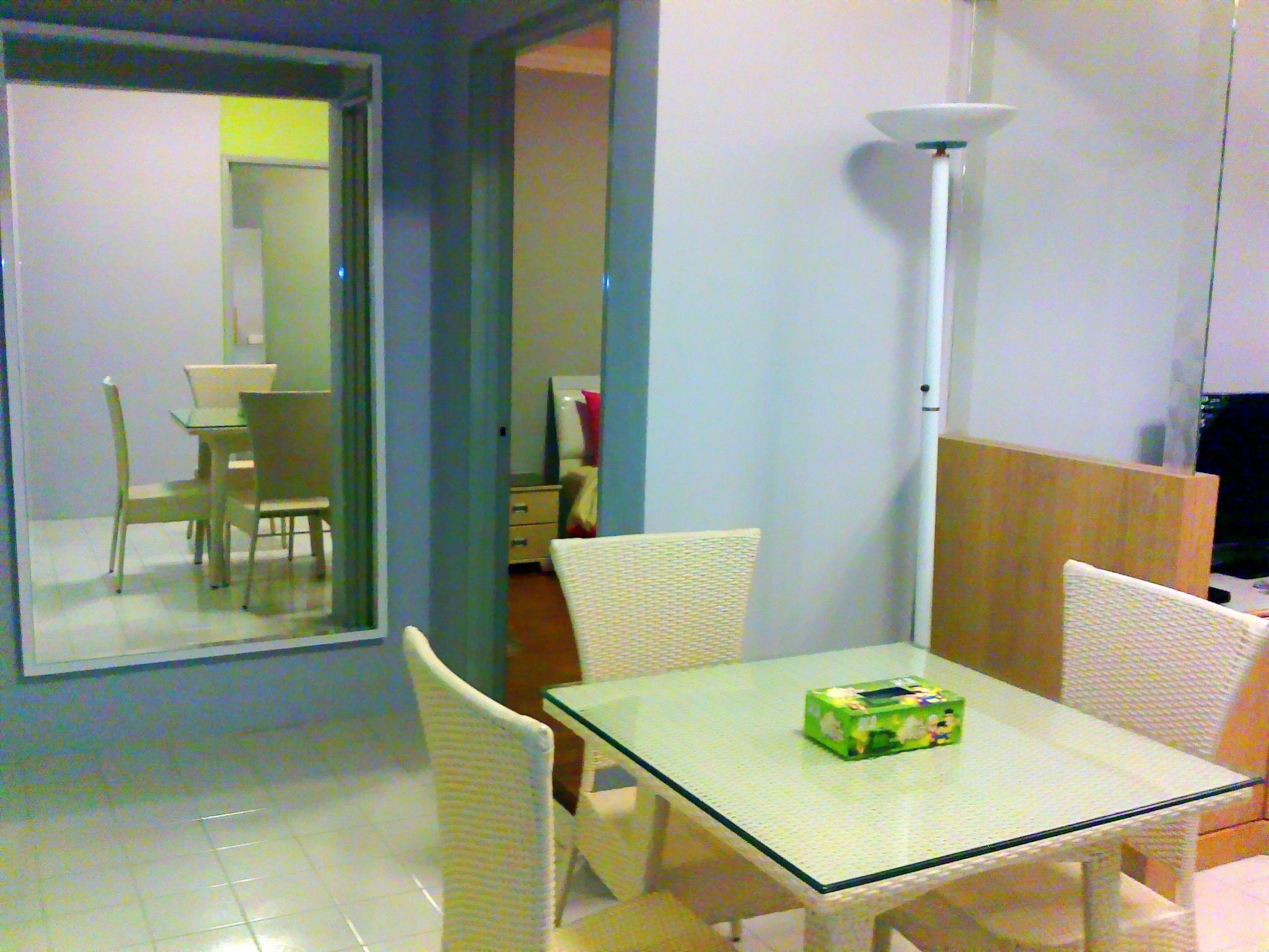 Ein Essbereich mit einem Glastisch und weißen Korbstühlen, einer weißen Lampe und einer Schachtel auf dem Tisch.