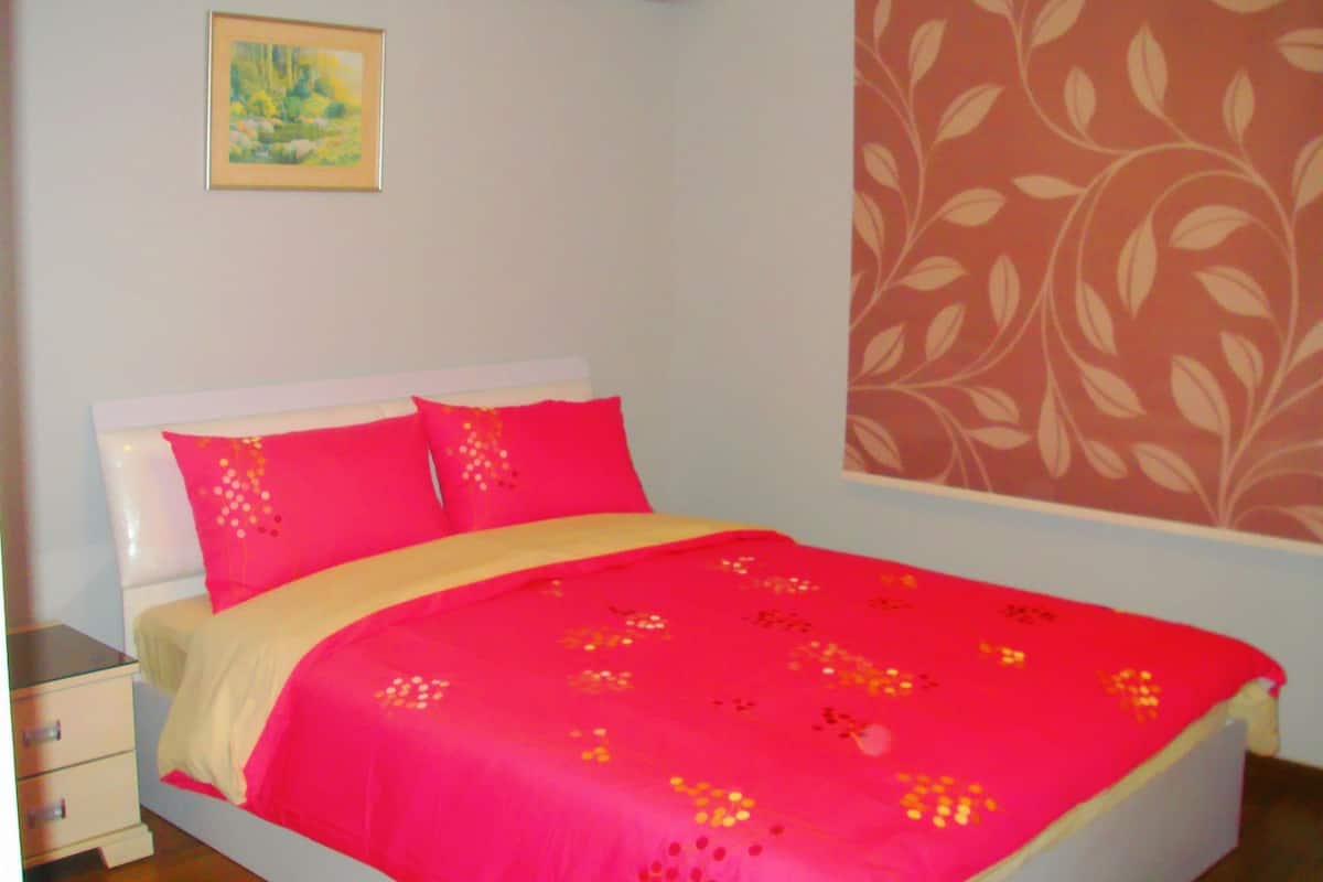A bedroom with a bed, pillows, a nightstand, a wall with a floral pattern, and a painting.