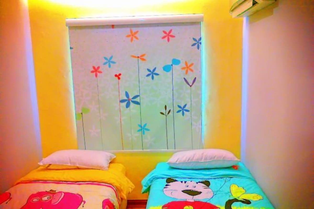 A room with two beds, each with a colorful bedspread. There is a window with a flower decal on the wall.