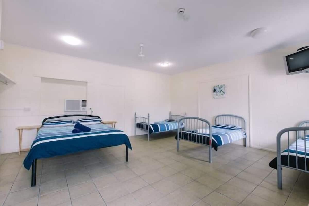 Habitación tipo dormitorio con tres literas metálicas, un televisor montado en la pared y una ventana con vistas al exterior.