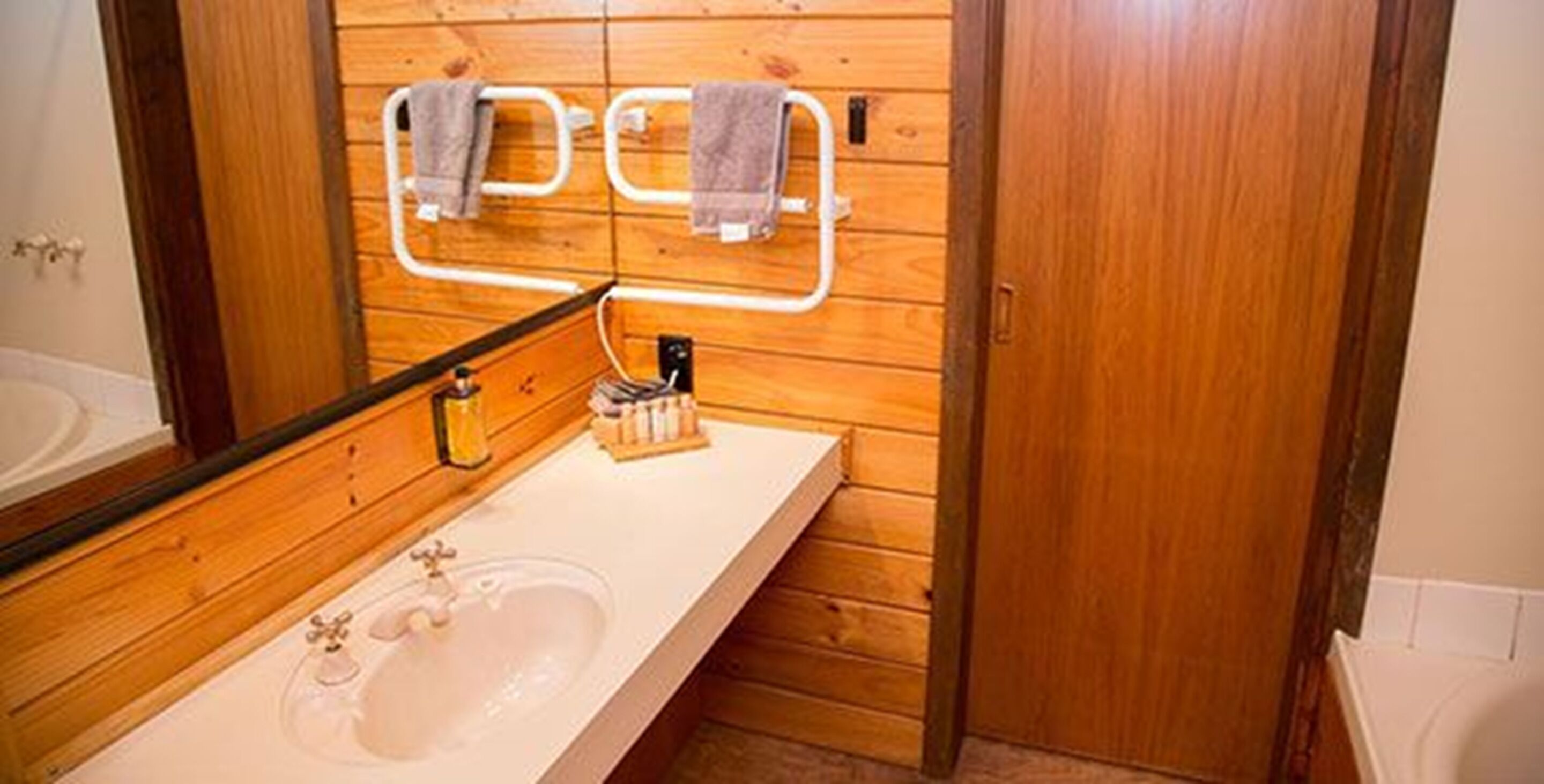A wooden-paneled bathroom with a white sink, a mirror, and towel hooks.