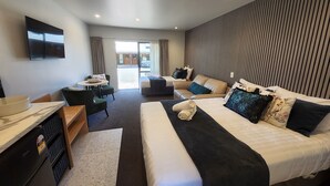 Quarto de hotel com duas camas, uma escrivaninha, uma cadeira e uma mesinha.