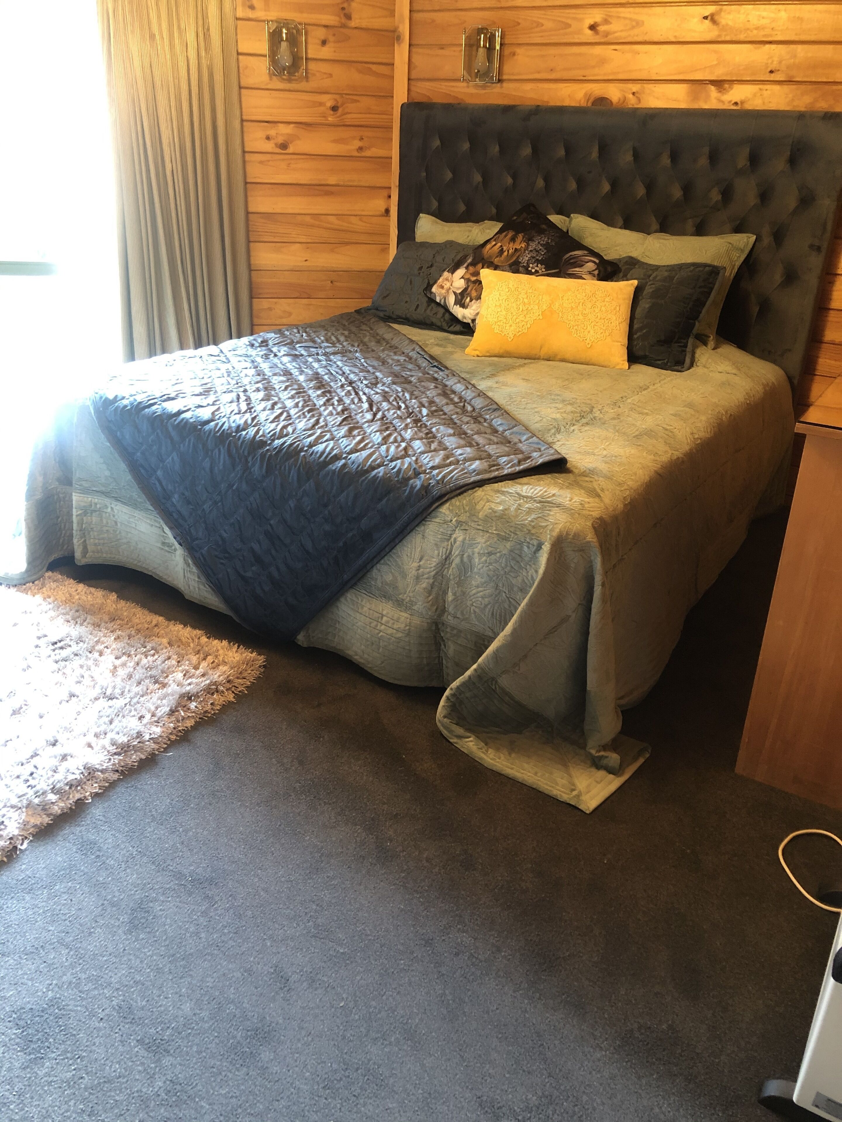 Una cama con colcha oscura, varias almohadas y cabecera de madera.