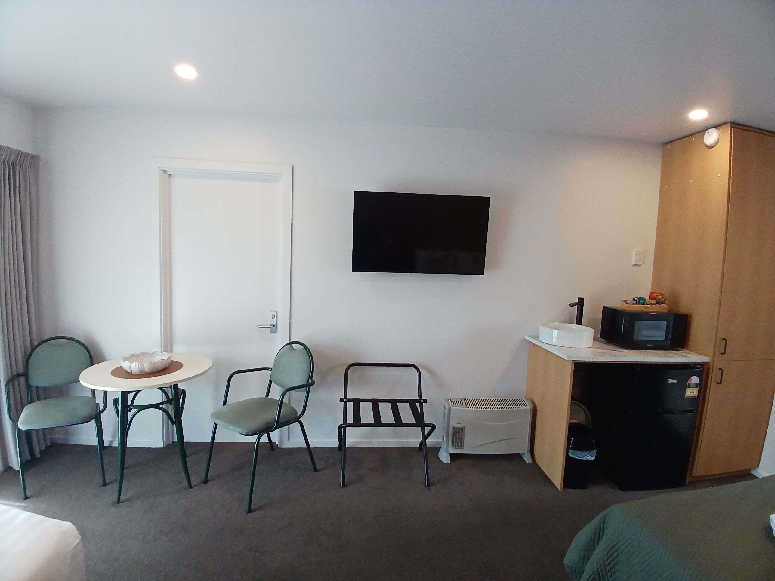 Een kleine hotelkamer met een bed, een eettafel met stoelen, een televisie, een magnetron en een koelkast.