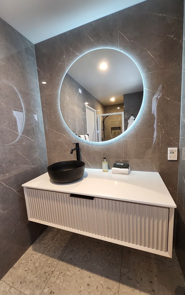 A modern bathroom with a large oval mirror, a black vessel sink, and a white vanity.