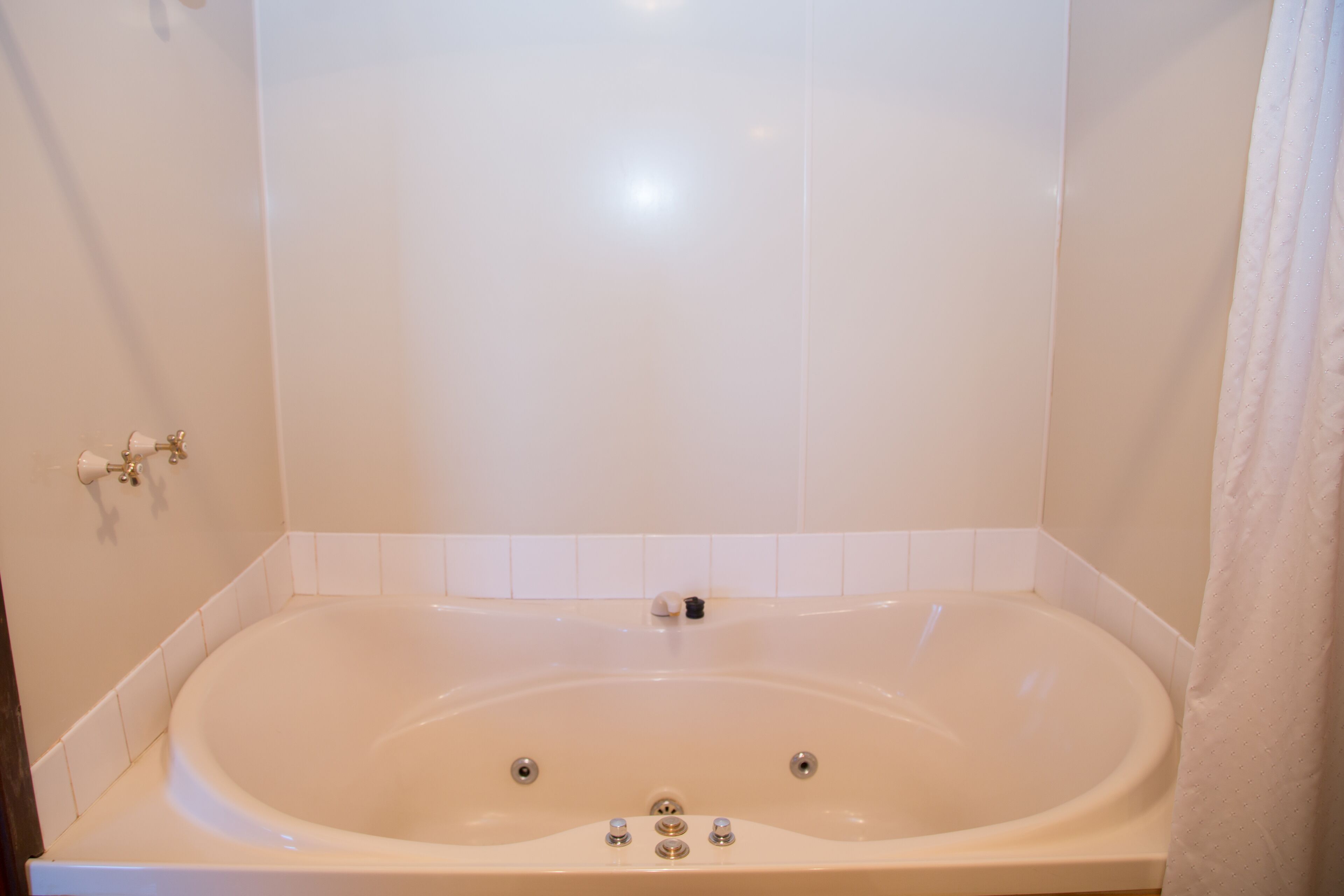Una tina grande independiente en un baño con azulejos blancos y una cortina.