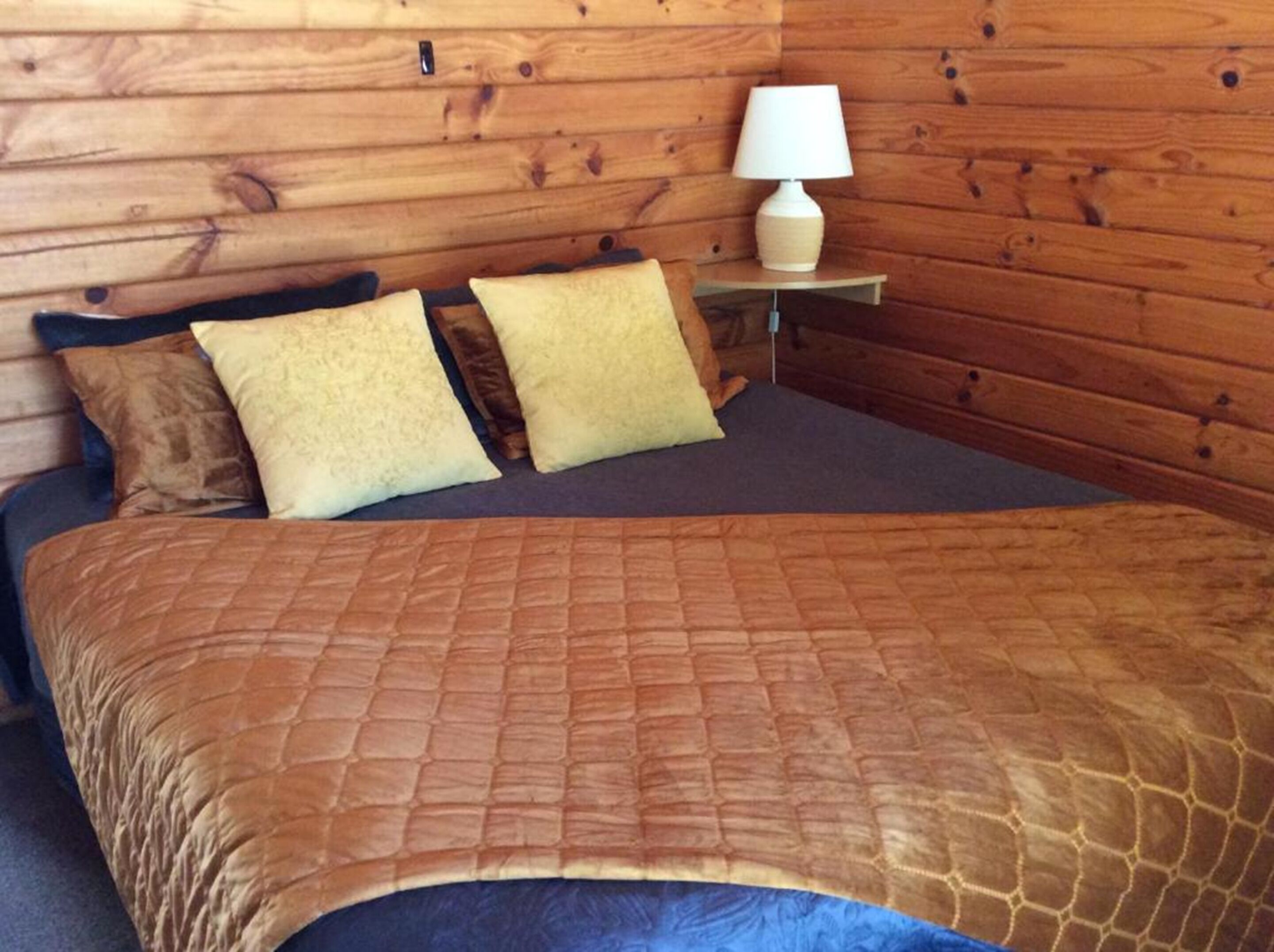 A bed with a brown quilt, two pillows, and a bedside table with a lamp.
