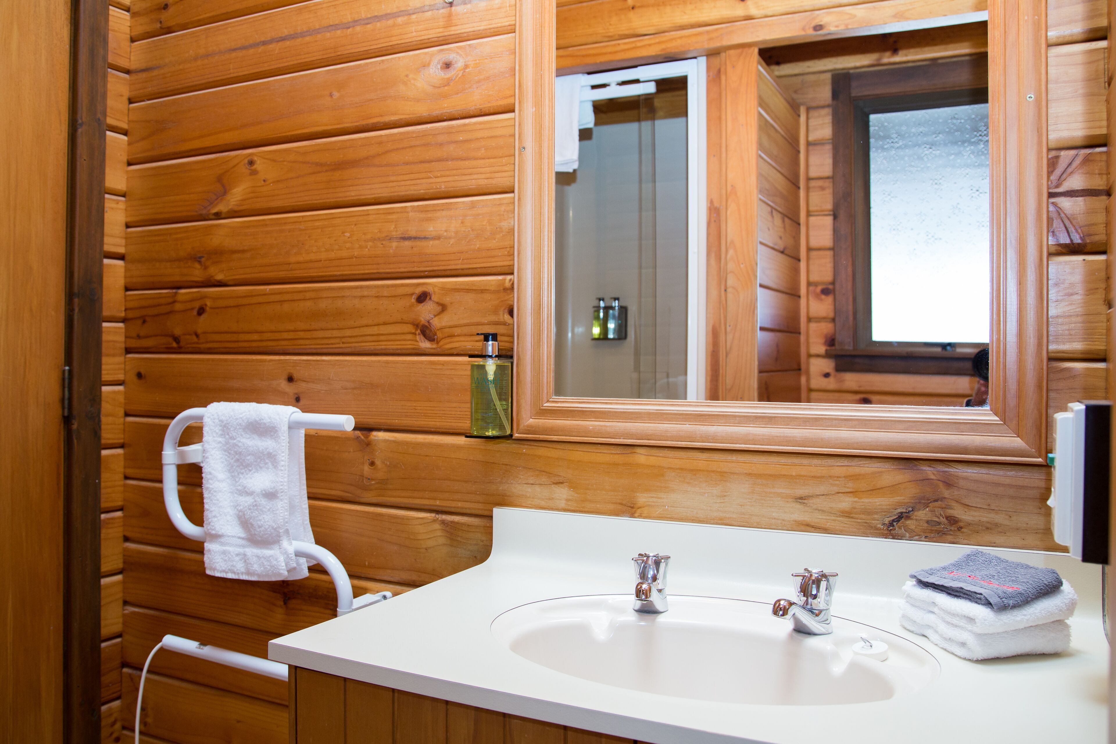 A wooden cabin bathroom with a white sink, two faucets, and a mirror.