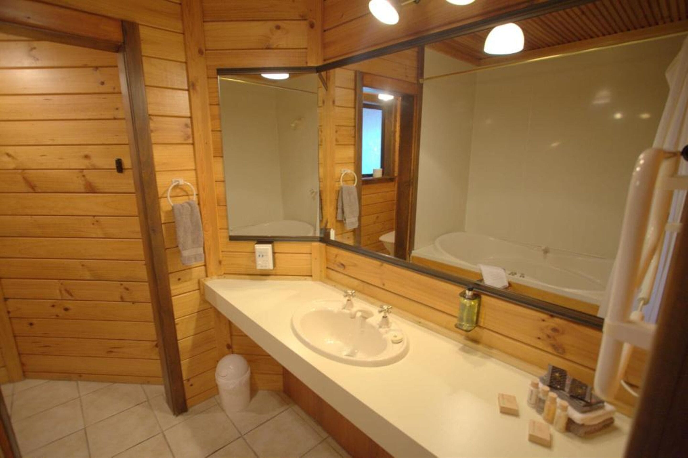 A wooden cabin bathroom with a large mirror, a sink, and a toilet.