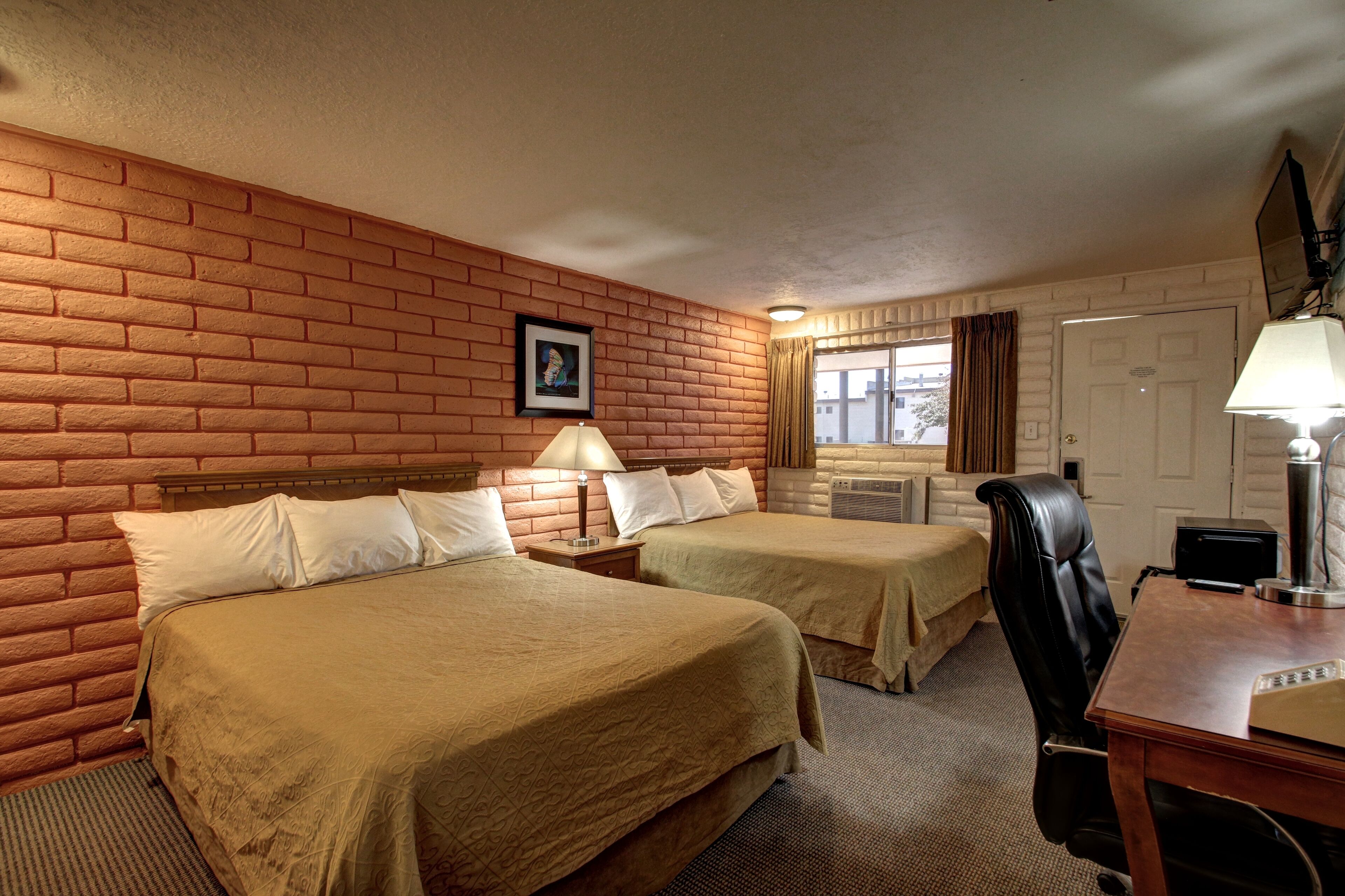 A hotel room with two beds, a desk, a chair, a lamp, and a picture on the wall.