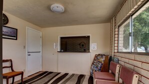 A room with a striped carpet, a door, a bench, a window with a brick wall, and a clock on the wall.