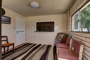A room with a striped carpet, a door, a bench, a window with a brick wall, and a clock on the wall.