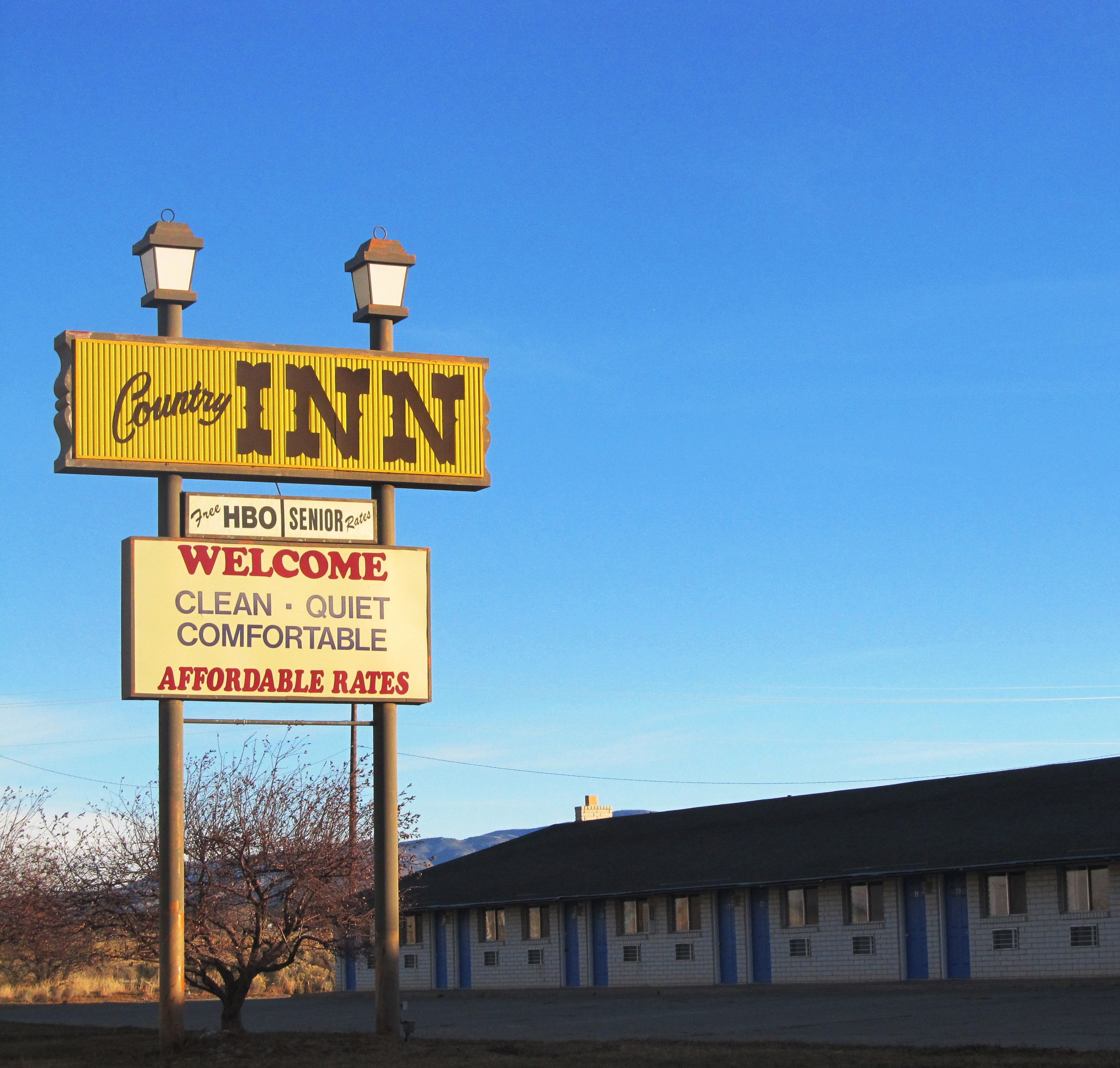 A Country Inn sign with a welcoming message and amenities like free HBO senior rates, clean, quiet, comfortable, and affordable rates.