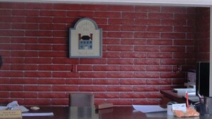 Zona de recepción con pared de ladrillo, un letrero de bienvenida, un escritorio con computadora y un pequeño cubo de basura.