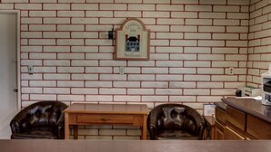 Una habitación con pared de ladrillo, una mesa de madera, dos sillones de cuero y un aparador de madera.