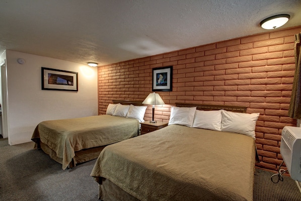 Habitación de hotel con dos camas, una pared de ladrillo y una lámpara en el techo.