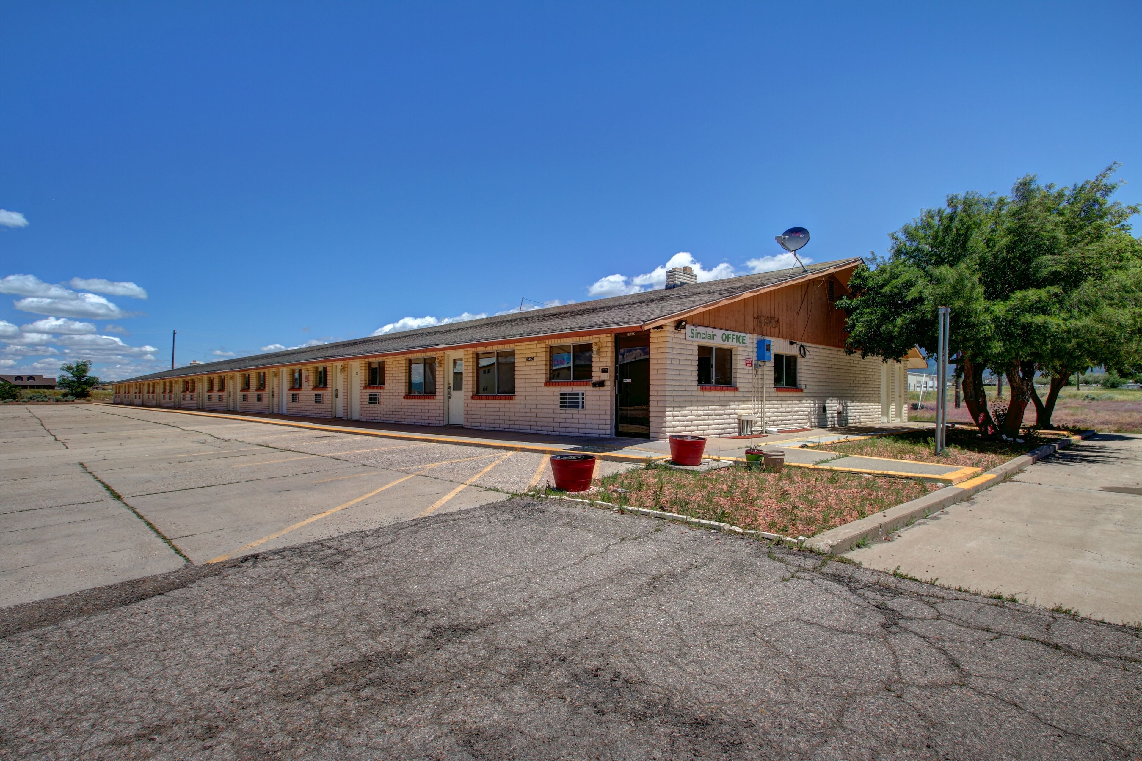 Un motel con una larga hilera de habitaciones, una pequeña recepción y un estacionamiento.