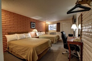 A hotel room with two beds, a desk, a chair, a lamp, a mirror, and a window with curtains.