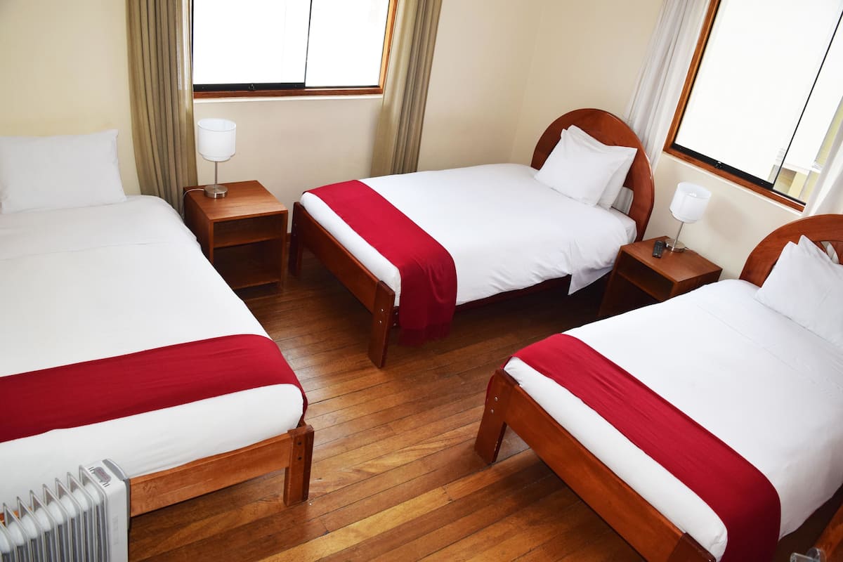Ein Hotelzimmer mit drei Einzelbetten, Holz-Kopfteilen, weißer Bettwäsche und Holzboden.
