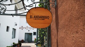 A wooden sign with "EL ANDARIEGO A HOME FOR THE JOURNEY" hanging on a metal structure. - El Andariego (Cusco)