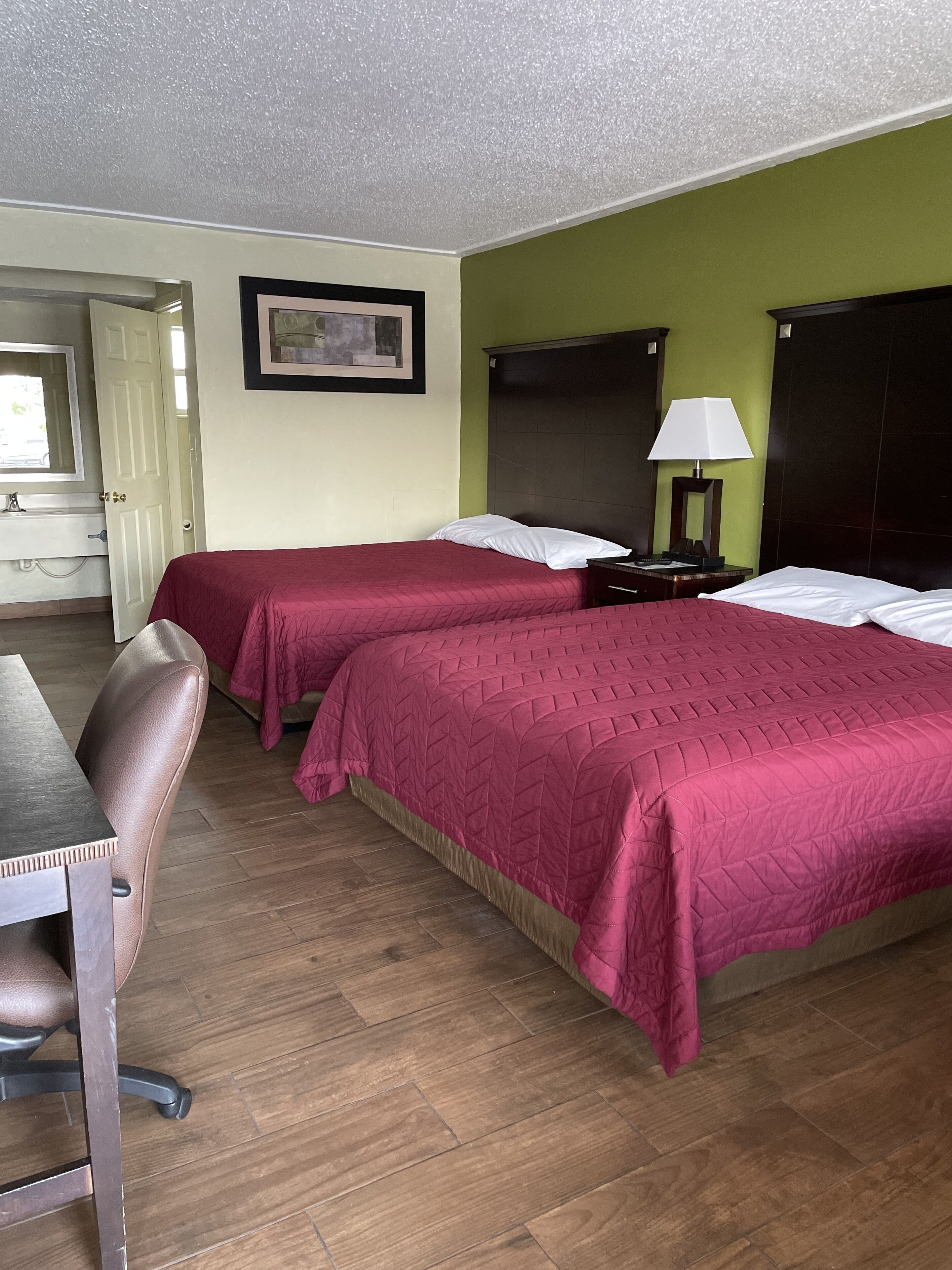 Habitación de hotel con dos camas, un escritorio, una silla, una mesita de noche, una lámpara y un cuadro en la pared.