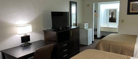 Habitación de hotel con escritorio, televisión, microondas, dos camas con ropa de cama estampada y un espejo.