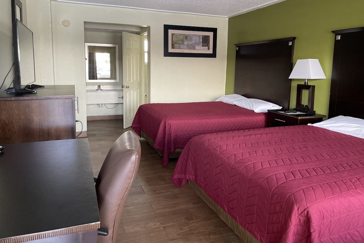 A hotel room with two beds, a desk, a chair, a desk lamp, and a mirror.