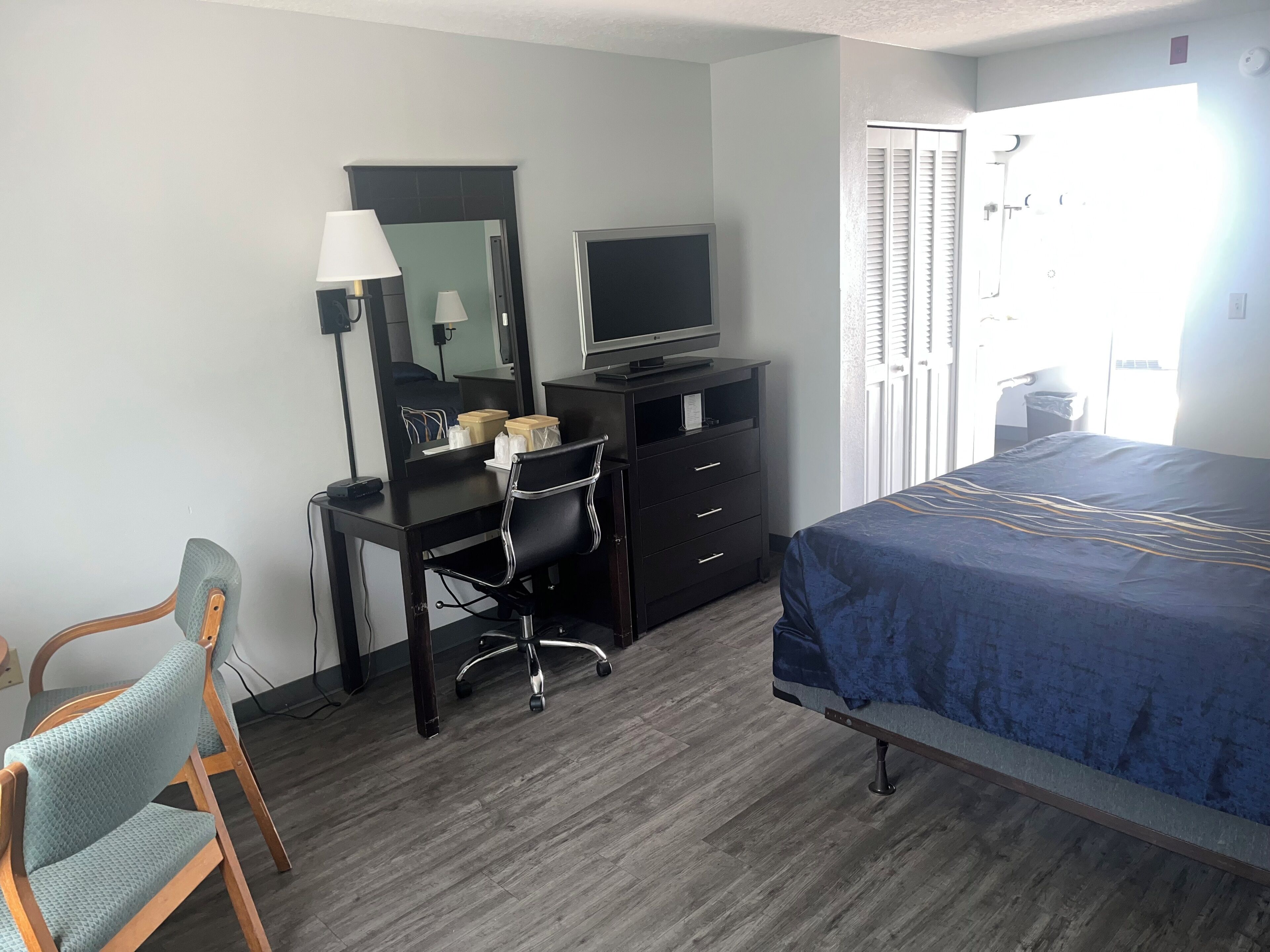 A hotel room with a bed, a desk with a computer, a chair, a TV, and a mirror.