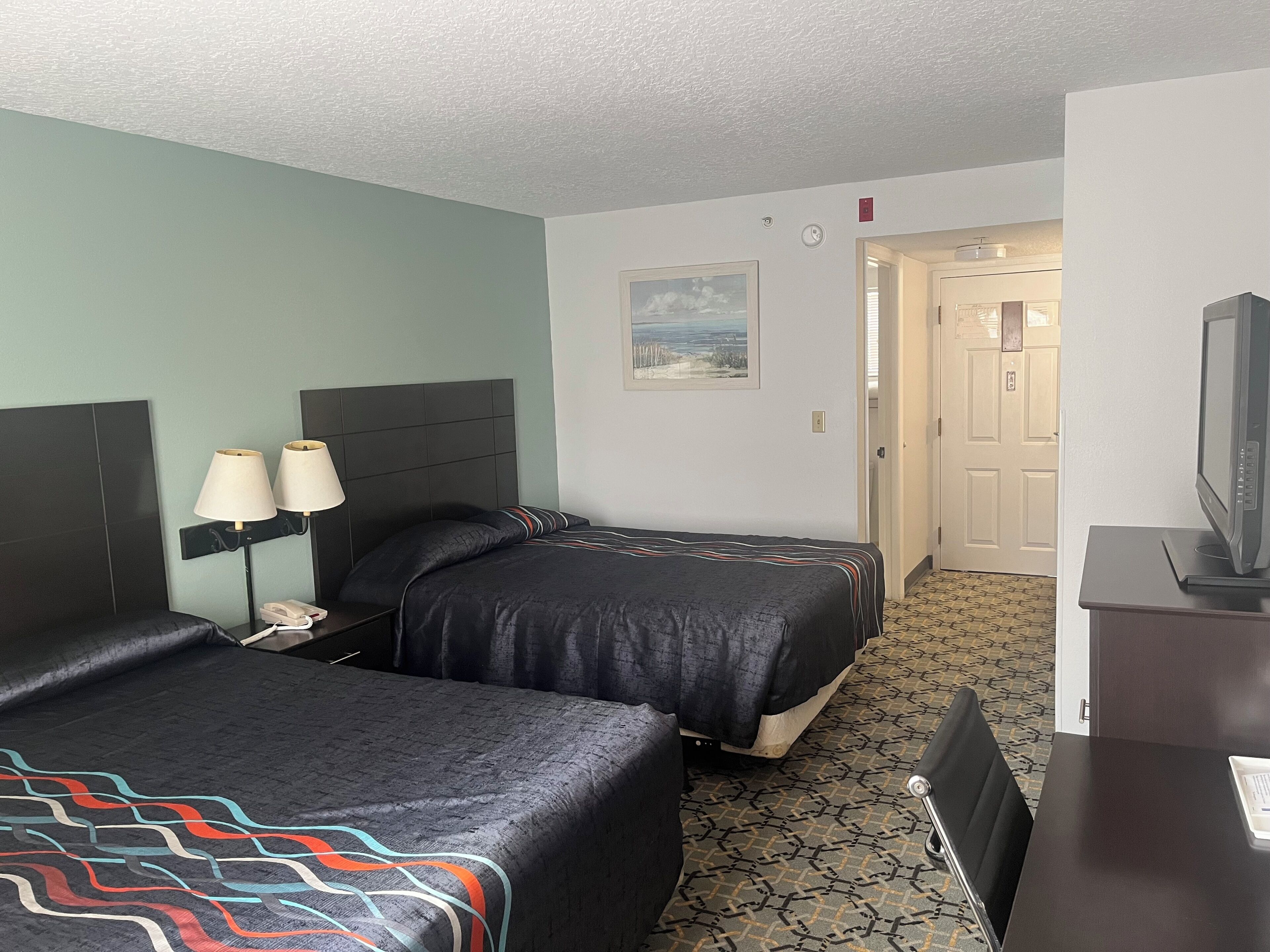 A hotel room with two beds, a desk with a television, and a door leading to another room.