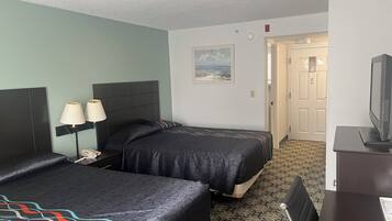 Een hotelkamer met twee bedden, een bureau met een televisie en een deur naar een andere kamer.